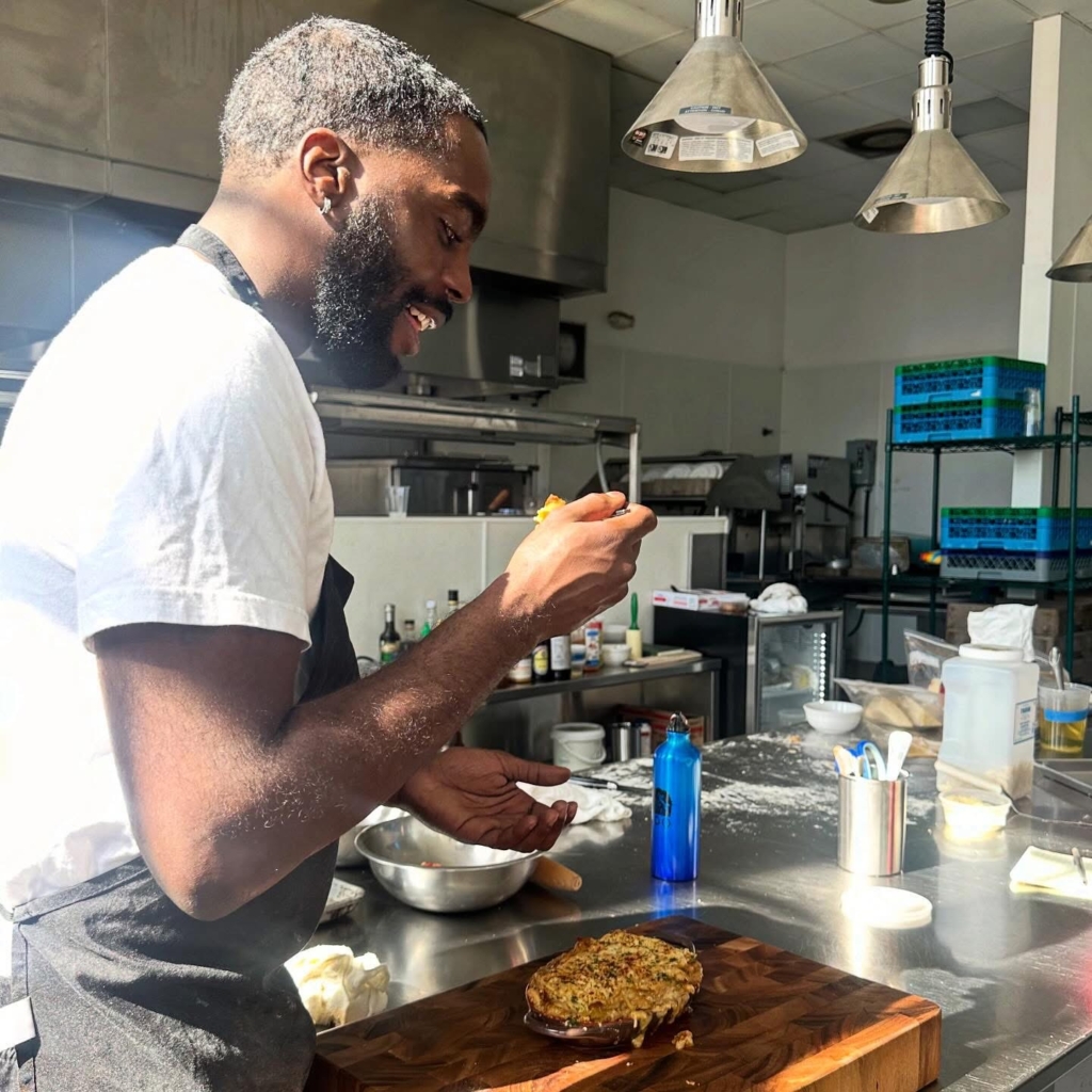 Rays from the morning sun rest on Hassan Gooden's back as he tries out the latest adjustment to his family-style seafood lasagna, which will be served in Velvet and Vine in March 2026. (Photo by Chanda Temple) 